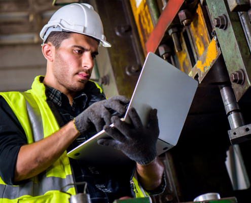 Engineer mechanic man checking for maintenance pressing metal machine by laptop at factory