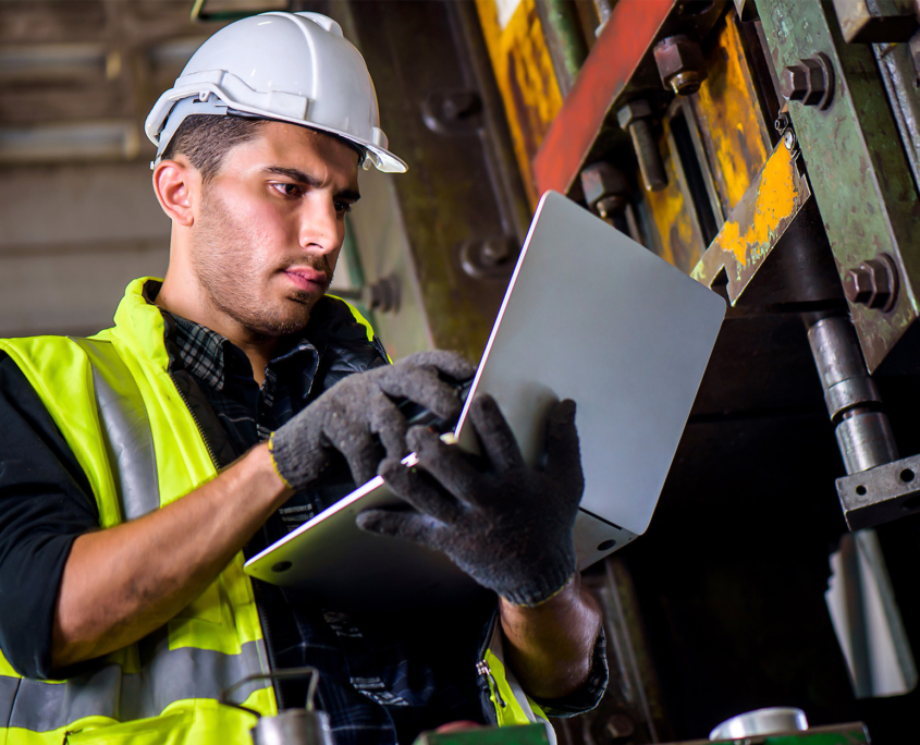 Engineer mechanic man checking for maintenance pressing metal machine by laptop at factory