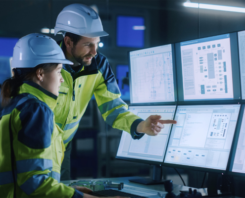 Side view of two engineers looking at six computer monitors